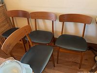 Four teak dining chairs grouped against a wall