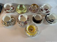 Nine assorted Aynsley tea cups with saucers laid out showing floral and decorative patterns.