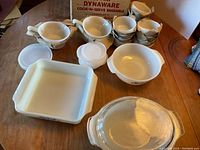 Complete view of the assortment of bakeware including square and round dishes, small dishes with plastic lids, and small pots with woven handle covers.