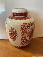Front view of the white porcelain pot with red Asian floral and ornate patterns, placed on a wooden surface.