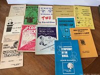 13 assorted magic books and pamphlets laid out on a flat surface showing cover titles and designs
