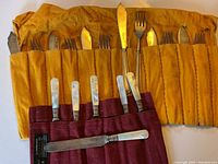Photo of assorted vintage sterling knives and forks stored in yellow and red fabric rolls.