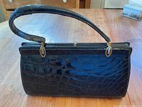 Front view of black purse showing crocodile embossed pattern and single strap handle.