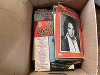 Box of assorted vintage sheet music and books showing titles like Sweet Caroline by Neil Diamond and Hi Parade book