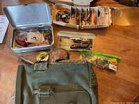 Top view of fishing bag, metal tackle box, multiple plastic lure boxes, fishing line spool, and bait pack on a table