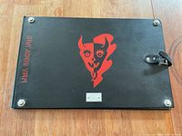 Top view of the closed black leather-bound book case with red Harley-Davidson logo and graphic centered, secured by latch and corner metal bolts.