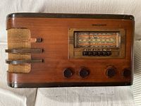 Front view showing wooden cabinet, fabric speaker grille with wood accents, tuning dial, push buttons and control knobs