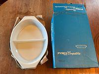 White Pyrex divided serving dish with two compartments and side handles next to original marked blue box.