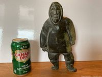 Front view of the carved soapstone figure next to a soda can for size reference, showing detailed clothing and face.