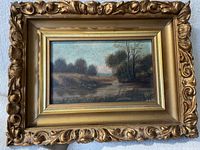 Framed landscape painting with ornate gilt frame, depicting a river or marsh scene with trees and grassy banks