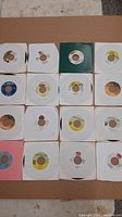 Top-down view of 16 assorted 7-inch reggae dancehall vinyl singles in white paper sleeves with various colored labels.