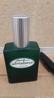 Front view of 1 oz Eddie Bauer Adventurer cologne showing the label on the green frosted glass bottle with a silver ribbed cap.