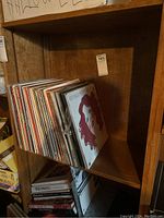 Shelf containing a vertical stack of assorted LP vinyl records, visible album cover with cartoon person with red curly hair and various spines with artist and album titles.