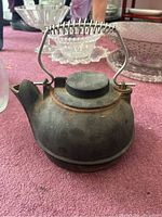 View of vintage cast iron tea pot with metal coil handle and slight rust on surface.