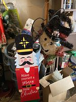 Wooden nutcracker figure with Christmas greeting text, hanging on a wall near other decorations.
