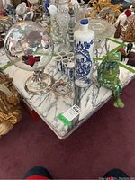 View of all items on a marble surface: Delft decanter and six cups, glass globe, sitting frog figurine, miniature quartz clock.