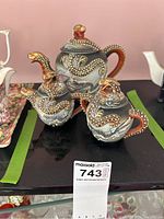Photo showing three ceramic teapots with dragon designs placed on black surface.