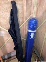 Two fabric bolts positioned upright against a wall: a black fabric bolt and a blue bubble wrap bolt wrapped in plastic.