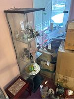 Glass display cabinet with black top and base, containing glass shelves. Various items seen inside but not included.