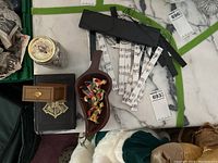 Photo showing entire lot items grouped on a surface: Harry Potter notebook, wooden leaf tray with clown miniatures, jar of coins, musical note wind chime with wooden hanger, black case holding Time Turner display box
