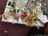 Table display of assorted Christmas decorations including ceramic houses, Santa and snowman figurines, gold floral ornament, artificial plants, and snow globe with Santa inside.
