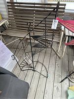 Wrought iron spiral staircase plant stand with decorative scroll accents on metal vertical supports, positioned on wooden deck with bench in background.