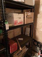 Full view of shelving unit with various boxes placed on shelves. Shelves are black metal frame with wood panel surfaces.