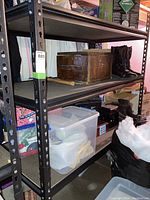 Steel shelving unit in basement with various items on shelves including plastic containers and boxes.