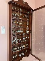 Front view of open wooden spoon display cabinet showing multiple rows of souvenir spoons inside.