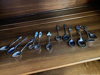 Full lineup of twelve sterling silver souvenir spoons showing variety in handle design and wear.