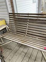 Wooden slat seat and backrest on a white metal pipe frame of the glider swing. Visible wear and weathering on the wood.