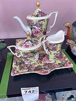 Porcelain tea set on black surface showcasing the teapot, sugar bowl, creamer, and rectangular tray with floral design.
