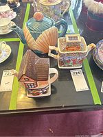Display of three assorted ceramic teapots on a black surface with green tape lines visible.