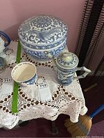 Photo showing the blue and white large covered bowl, teapot, and teacup on a lace tablecloth