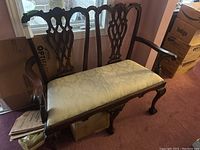 Full side angle showing detailed carved back and armrest with upholstered cream seat cushion.