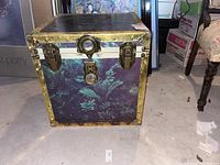 Front view of the square vintage trunk highlighting the brass latches and fern-patterned exterior.