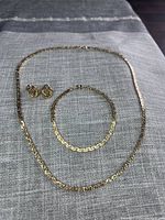 Photo showing the entire set on a grey textured fabric background with necklace, bracelet, and earrings visible.