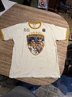 White vintage t-shirt laid flat on table showing front graphic of two men in California Highway Patrol uniforms, text 'RINGSPUN ALLSTARS' and number 55.