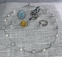 Photo showing the 6-piece lot of costume jewelry on grey fabric background including 16-inch Monet necklace with pearl and rhinestone accents and 5 assorted rings and earrings