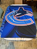 Vancouver Canucks fleece throw blanket laid flat on a table showing prominent team logo and colors.