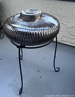 Black ribbed ceramic fire pot atop a black wrought metal stand, shown from an angled side view on a patio surface.