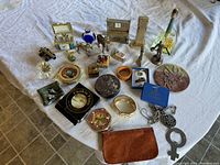 Wide view of the lot showing variety of vintage items including boxes, figurines, jewelry, and decorative pieces arranged on a white cloth.