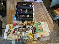 Flambeau plastic tackle box with open trays showing fishing tackle and various fishing accessories spread out on table