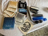 Lot contents including harmonicas, guitar strings, and microphone on a fabric surface.