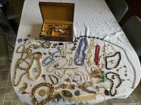 Full display of assorted vintage costume jewelry including necklaces, bracelets, rings, brooches displayed on a table with the cedar box behind.