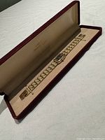 Overall view of ladies Bulova watch in velvet-lined jewelry box showing full watch length, decorative gold-tone link bracelet, rectangular black face with gold hands and markers.