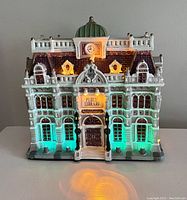 Front view of the Lemax Public Library model lit with warm green lighting from inside windows and signage.