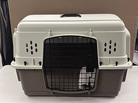 Full view of the small dog crate showing beige top, dark brown base, and black front door with grid style metal bars.