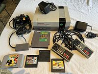 Nintendo Entertainment System console with power adapters, NES controllers, and game cartridges including Donkey Kong Country and Sega games arranged on table.
