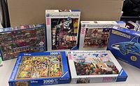 Photo of six Ravensburger puzzle boxes stacked and laid out showing variety of scenes and 1000 piece labels